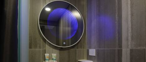 A modern bathroom with a round mirror, a white sink, and two small shelves.