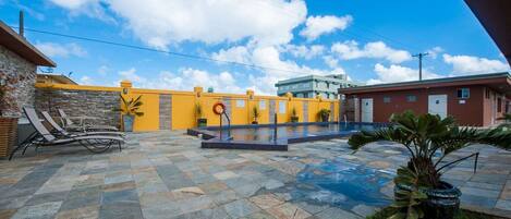 A courtyard with a swimming pool, lounge chairs, and a stone-tiled floor.