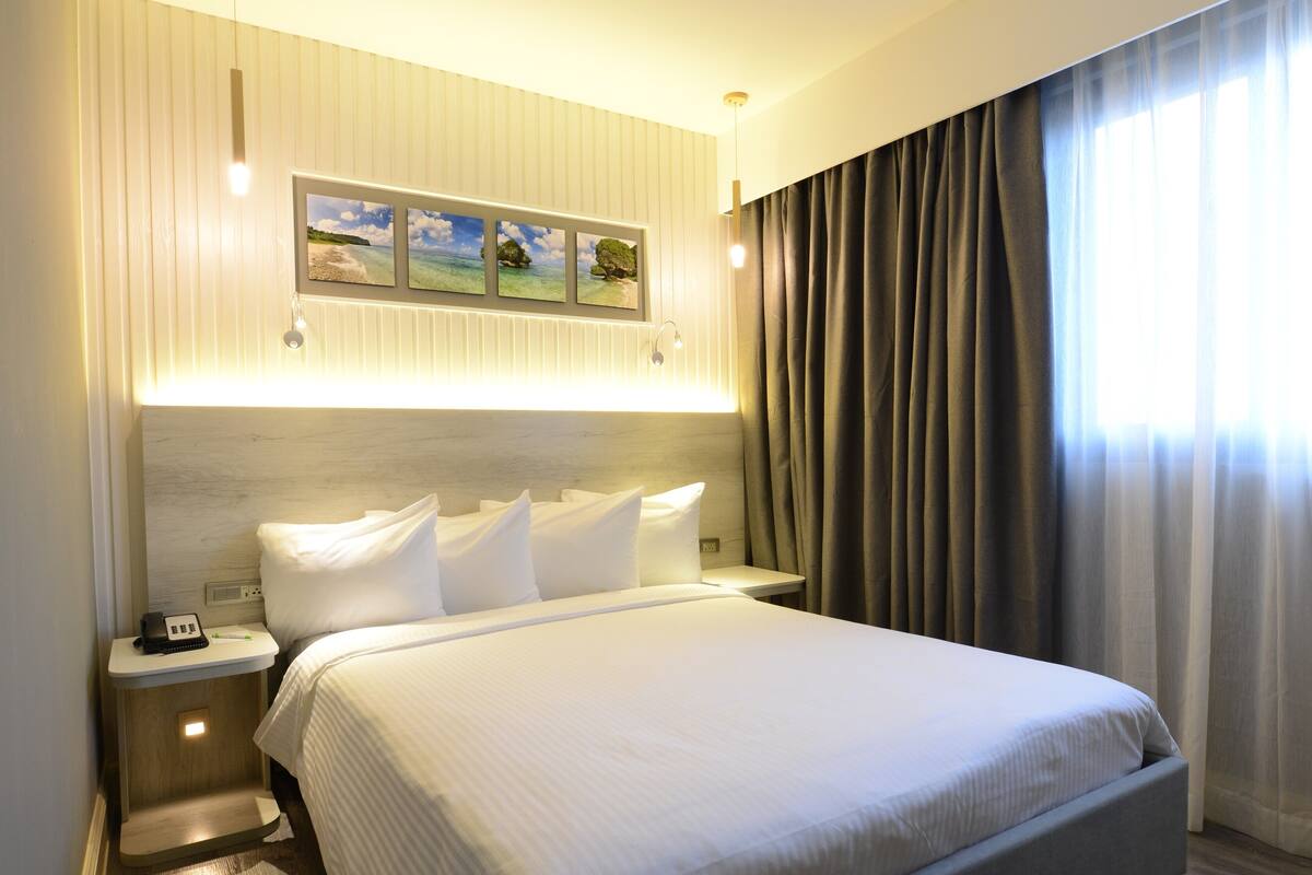 Ein modernes Hotelzimmer mit einem großen Bett, einem Nachttisch mit Telefon und einem Wandbild.