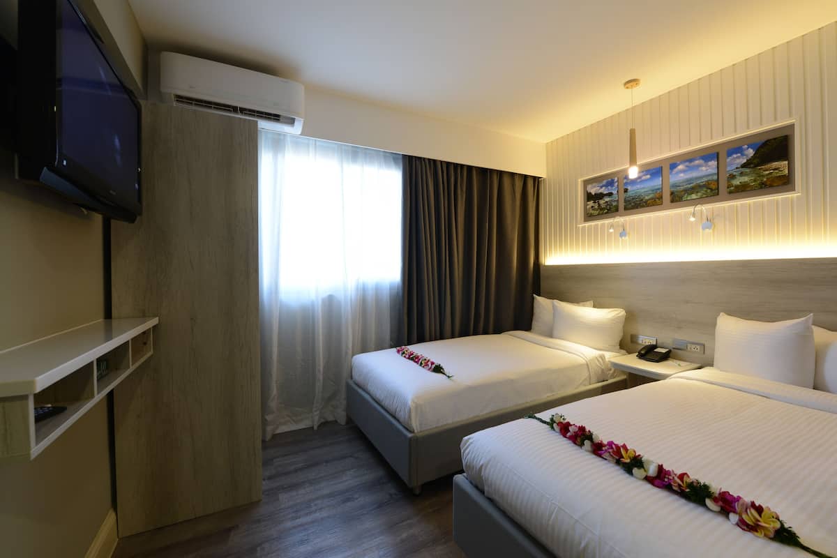Ein Hotelzimmer mit zwei Betten, einem Fernseher, einer Klimaanlage, einem Nachttisch mit Telefon und einem an der Wand hängenden Bild.