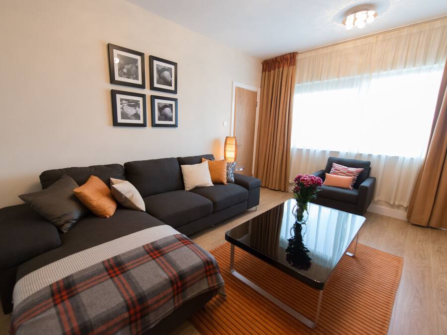 Una sala moderna con un sofá oscuro, un plaid y una mesa de centro de vidrio.