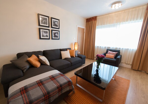 Una sala moderna con un sofá oscuro, un plaid y una mesa de centro de vidrio.