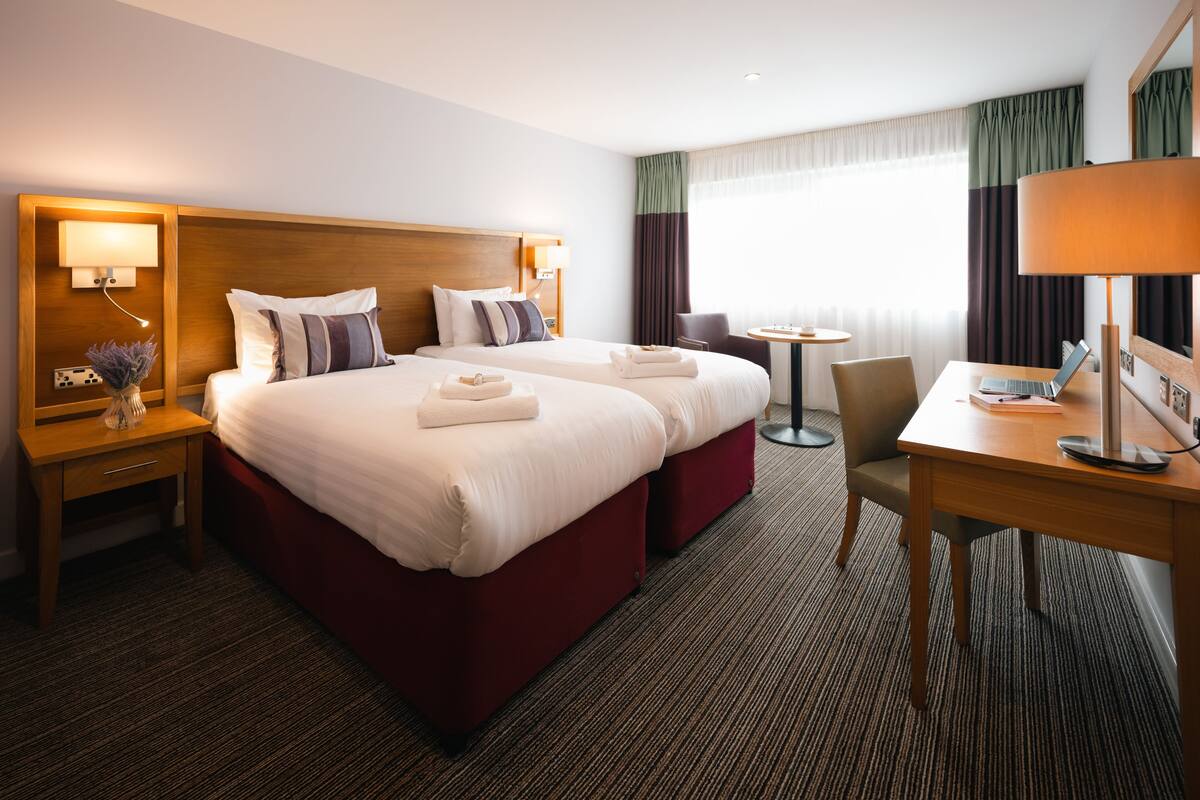 Une chambre d’hôtel avec deux lits, un bureau, une chaise et une petite table.