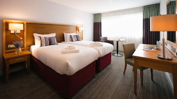 A hotel room with two beds, a desk, a chair, and a small table.