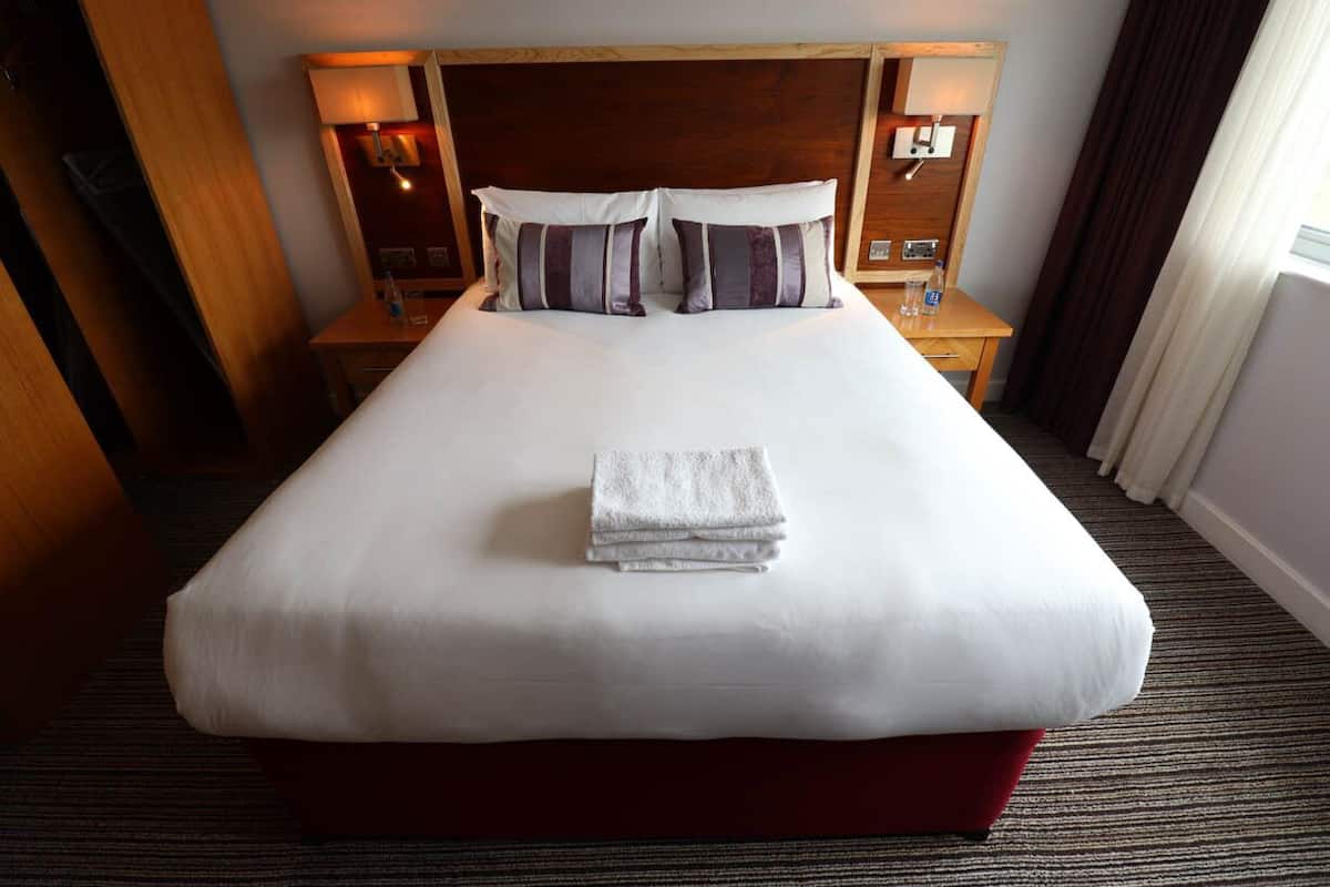 Une chambre d’hôtel avec un grand lit, deux tables de chevet et une tête de lit dotée d’un éclairage intégré.