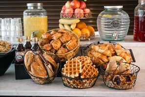 Un buffet de petit-déjeuner proposant un assortiment de viennoiseries, de pains, de gaufres et de fruits.