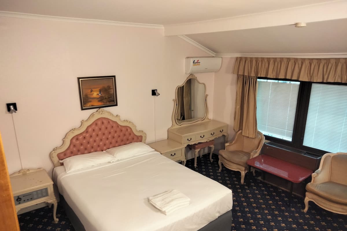 A hotel room with a large bed, a desk, a chair, and a window with blinds.