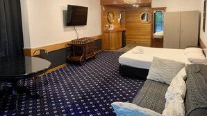 A hotel room with a bed, a sofa, a desk with a television, a wardrobe, and a chandelier.