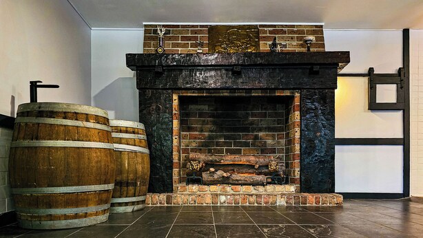 A fireplace with a brick surround, two wooden barrels, and a tiled floor.