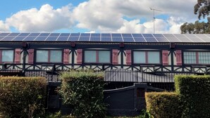 A building with a solar panel roof, a Tudor-style facade, and a gated entrance.