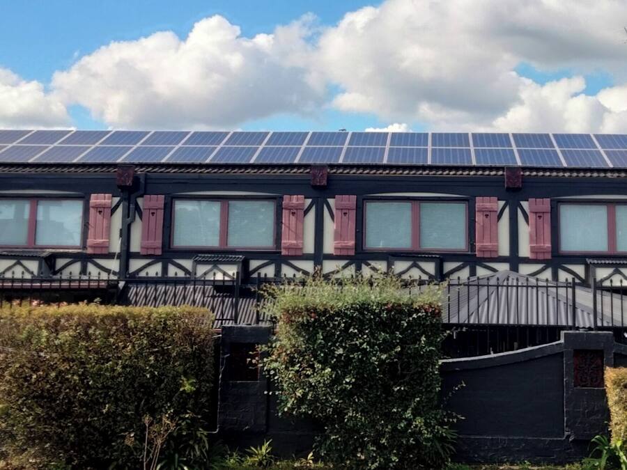 Un bâtiment doté d’un toit recouvert de panneaux solaires, d’une façade de style Tudor et d’une entrée sécurisée par un portail.
