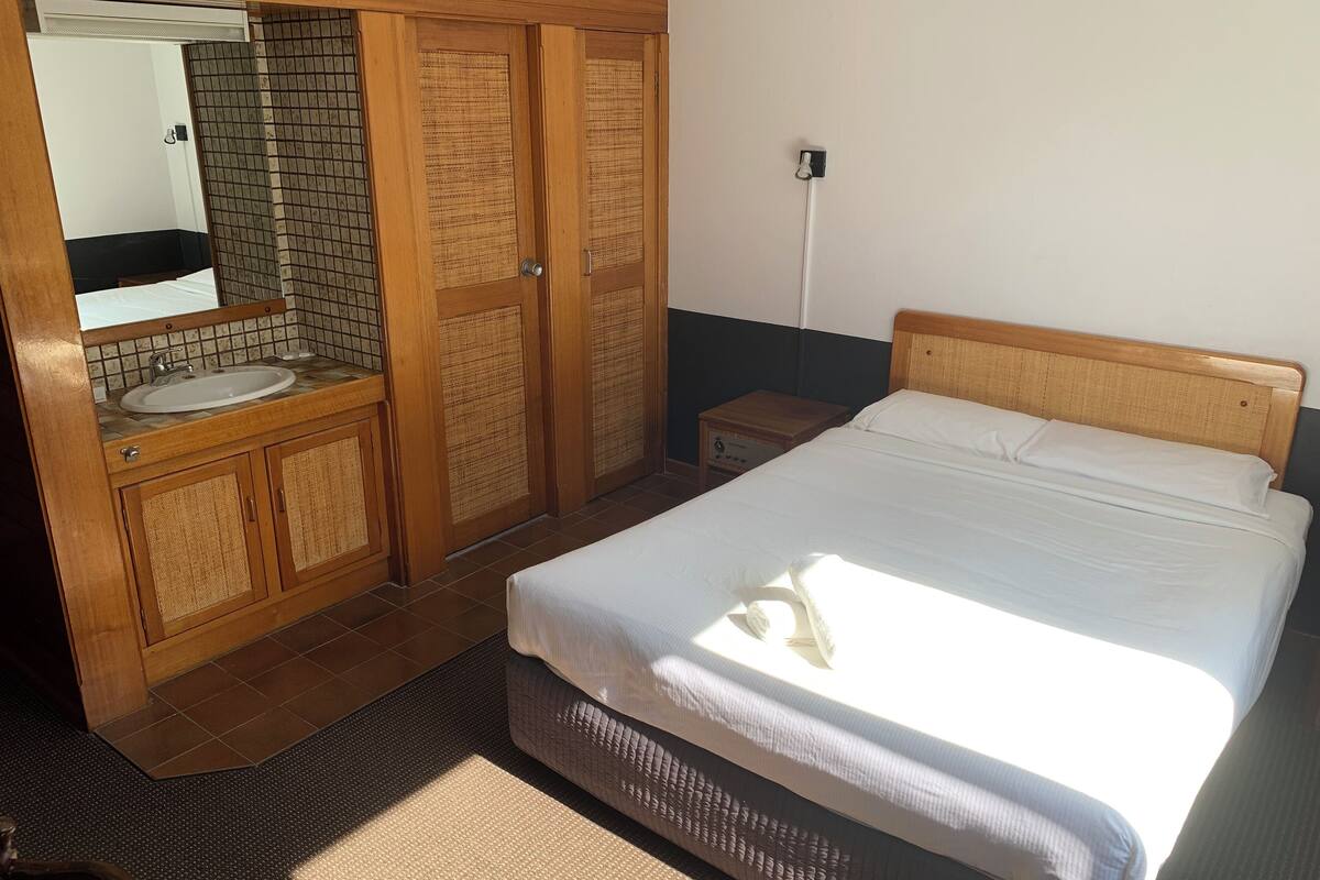 A bedroom with a bed, wooden wardrobe, and a bathroom with a sink and mirror.