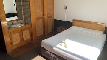 A bedroom with a bed, wooden wardrobe, and a bathroom with a sink and mirror.
