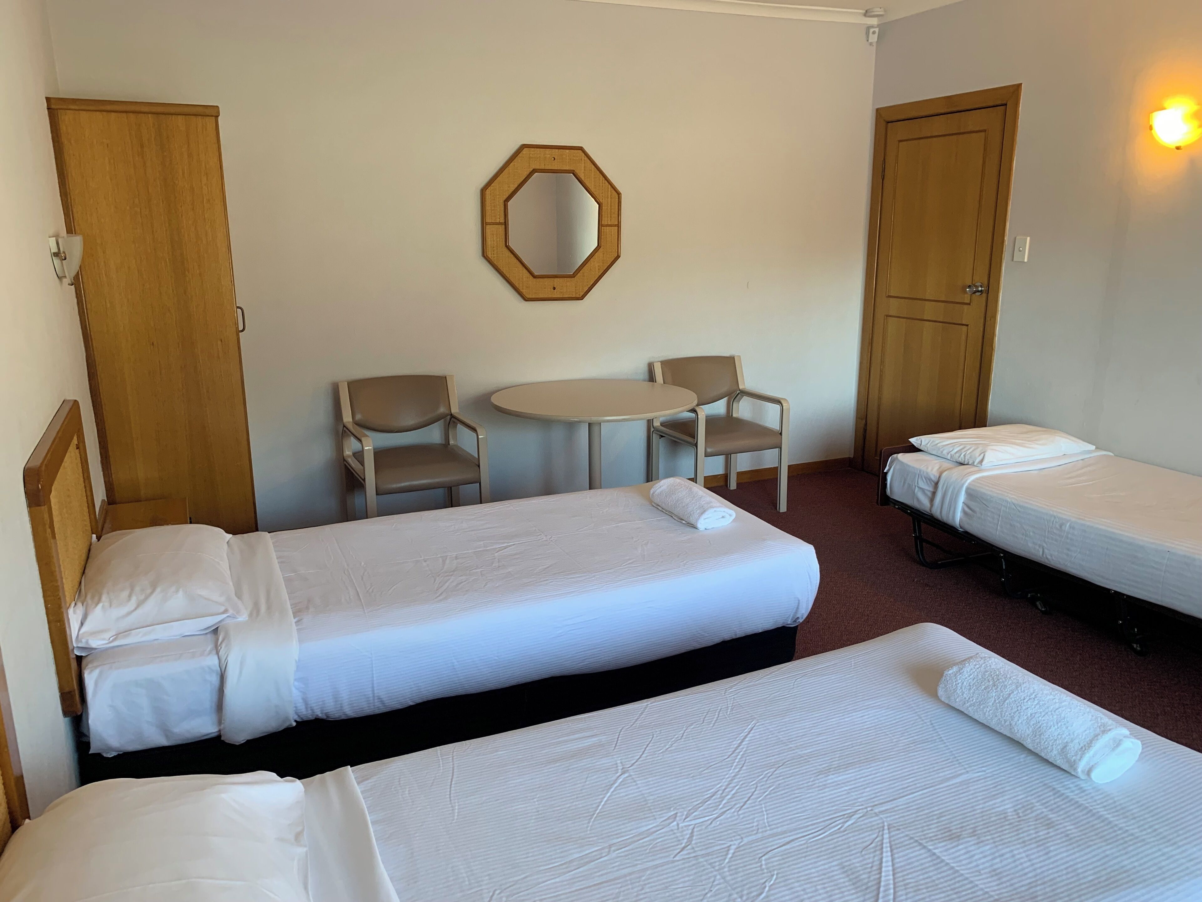 A hotel room with two single beds, a round table, two chairs, and a mirror on the wall.