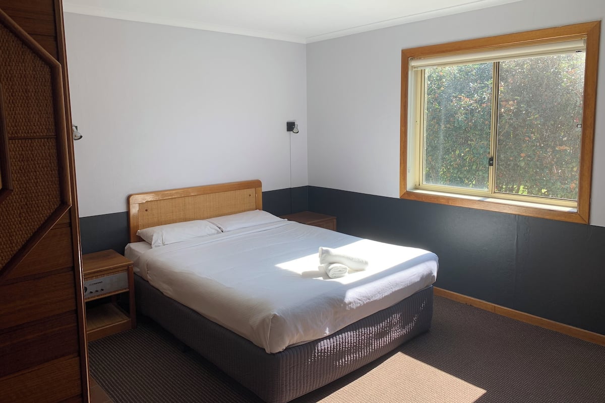 A bedroom with a bed, a nightstand, a window, and a door.