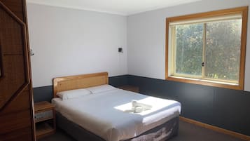 Un dormitorio con cama, mesita de noche, ventana y puerta.