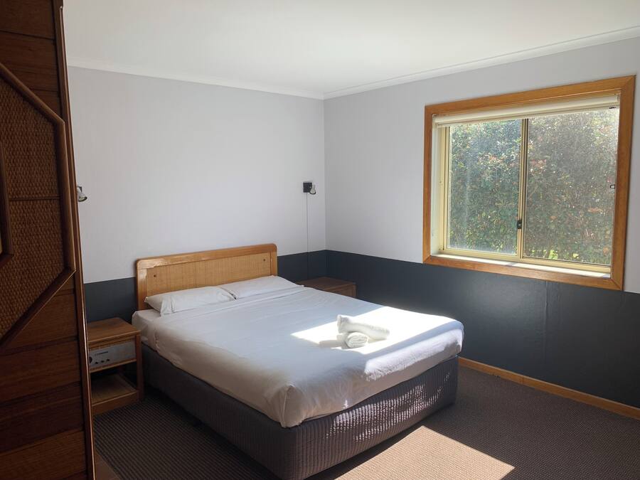 Un dormitorio con cama, mesita de noche, ventana y puerta.