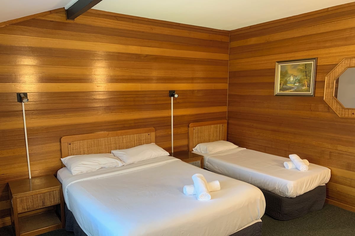 A hotel room with two beds, wooden paneling on the walls, a painting, and a mirror.