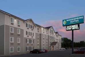 Un hôtel à plusieurs étages, avec une enseigne indiquant qu’il s’agit d’un hôtel Woodspring Suites proposant des séjours de longue durée.