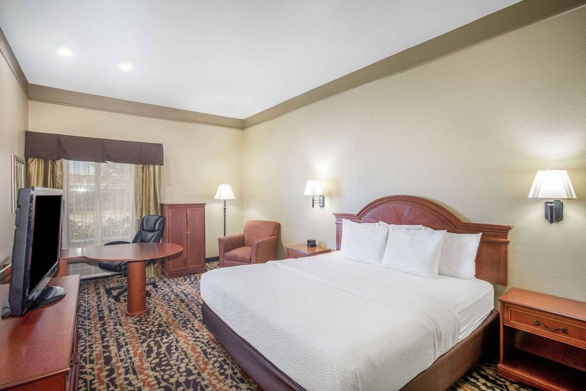 Habitación de hotel con cama, escritorio con computadora, silla, televisor y ventana con cortinas.
