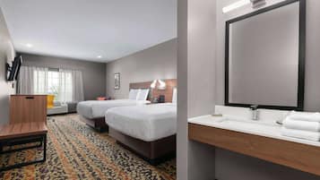 A hotel room with two beds, a desk, a large mirror, and a bathroom with a sink and towel rack.