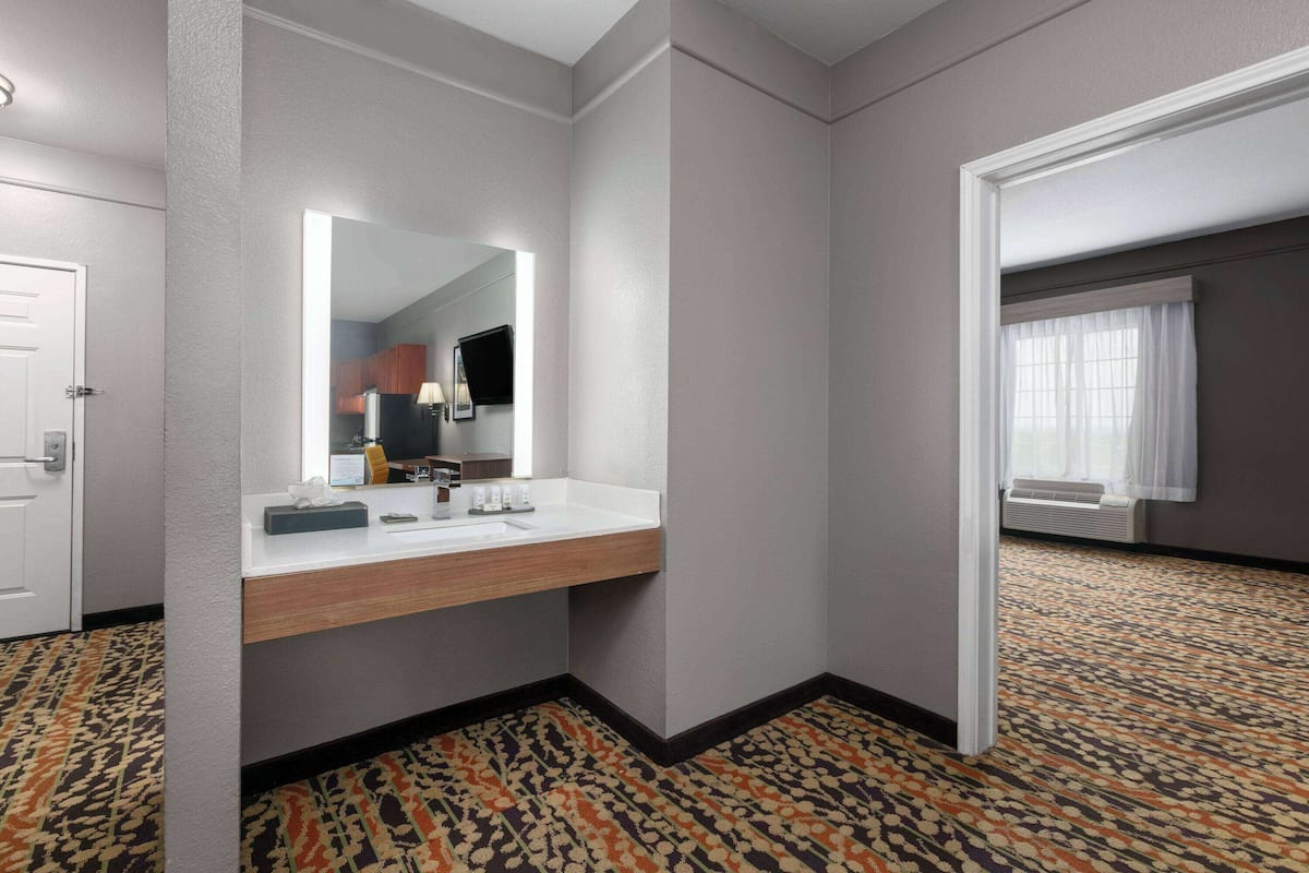 A hotel bathroom with a large mirror, a sink, and a patterned carpet.