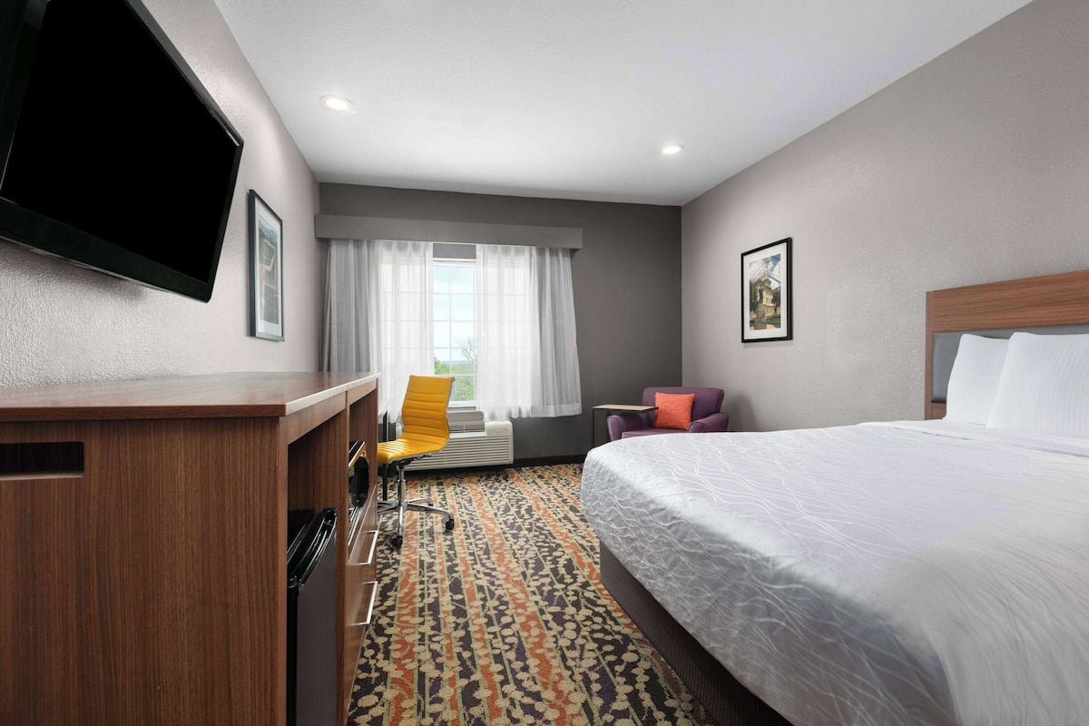 A hotel room with a bed, a desk with a chair, a television, and a window with curtains.
