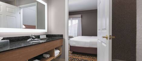 A hotel bathroom with a sink, mirror, and a bed.
