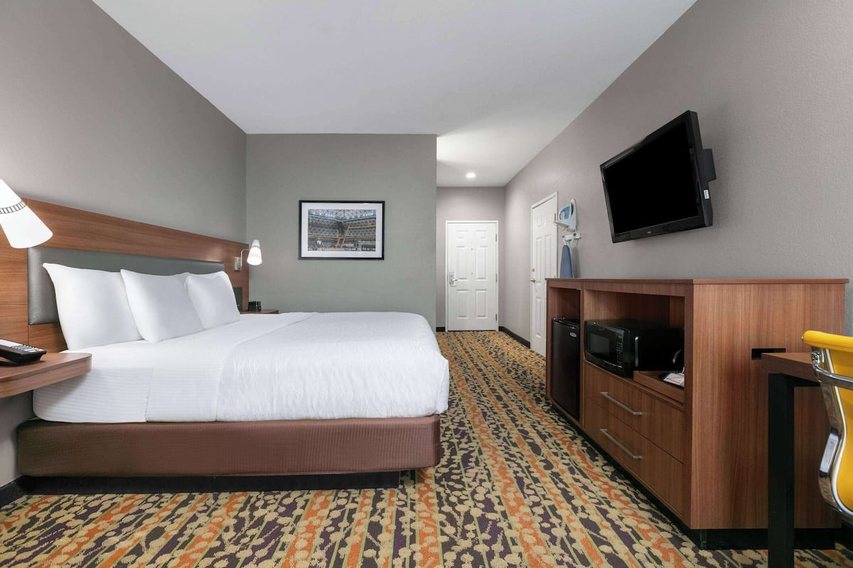 A hotel room with a bed, a desk with a lamp, a television, a microwave, and a door.
