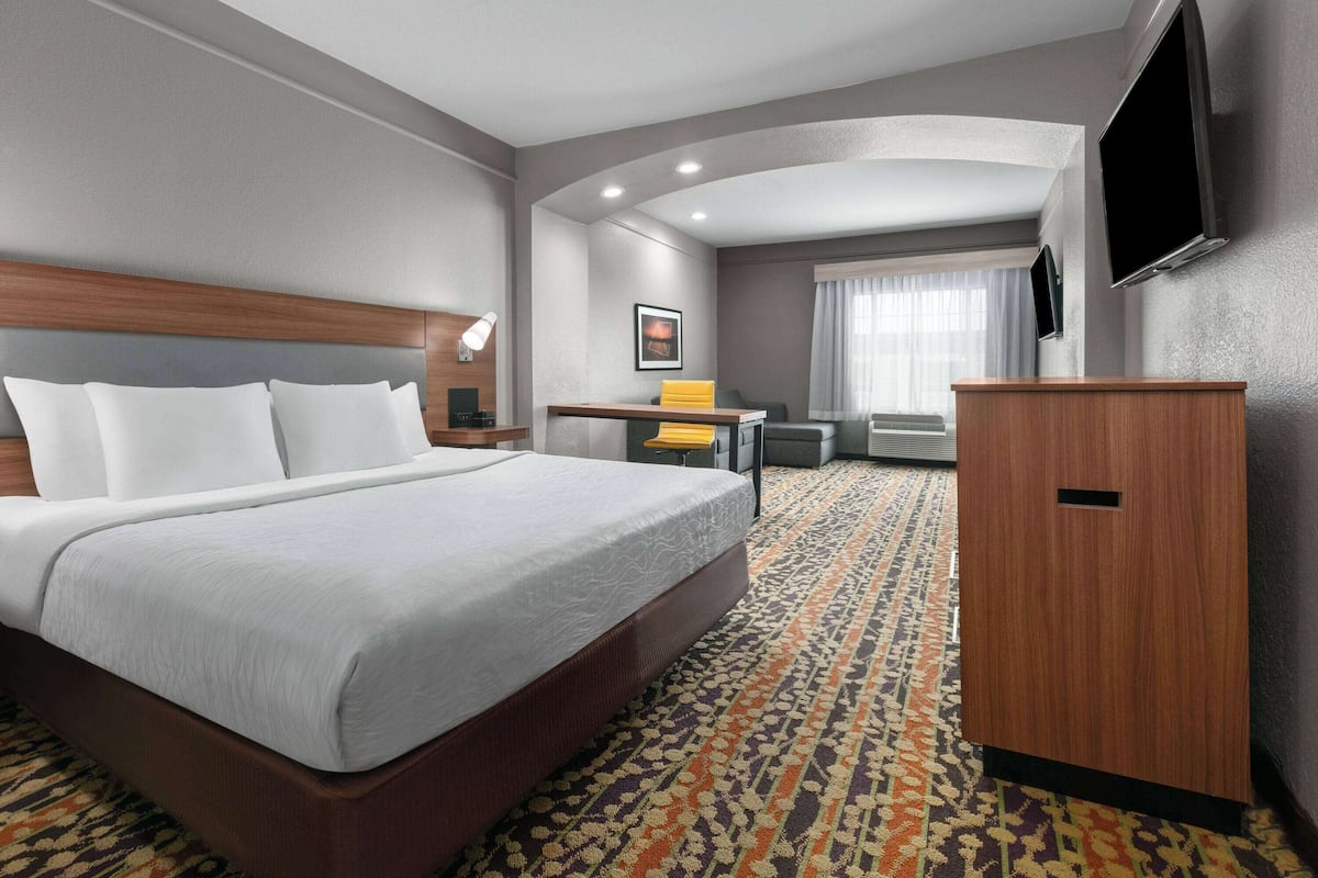 A hotel room with a large bed, a desk, a chair, a television, and a wardrobe.