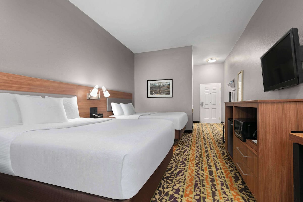 A hotel room with two beds, a TV, a desk, and a patterned carpet.