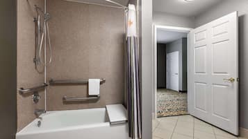 A bathroom with a bathtub, shower, grab bars, and a towel rack.