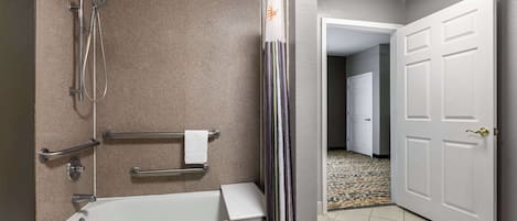 A bathroom with a bathtub, shower, grab bars, and a towel rack.