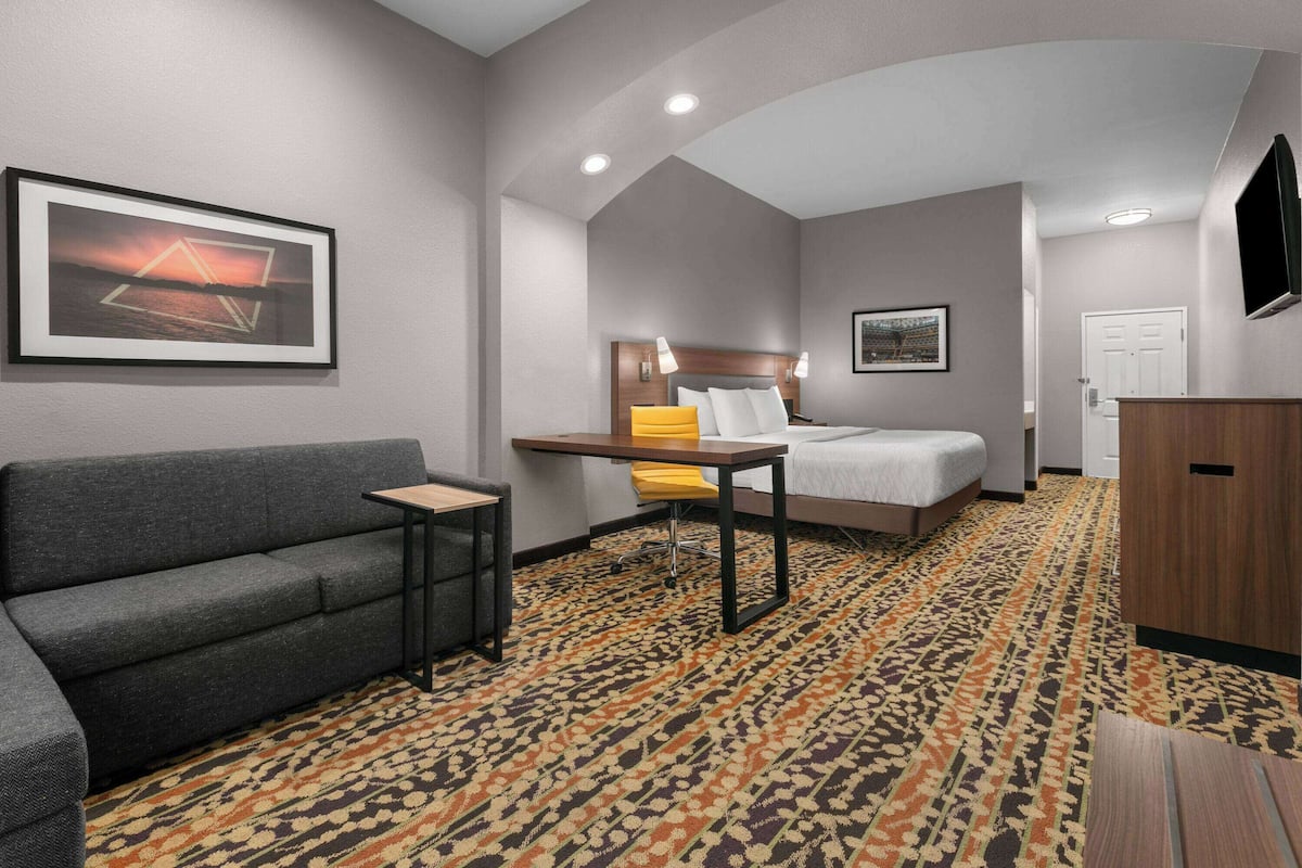 A hotel room with a sofa, a small table, a bed, a desk, and a patterned carpet.
