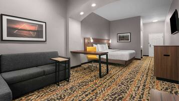 Une chambre d’hôtel avec un canapé, une petite table, un lit, un bureau et une moquette à motifs.