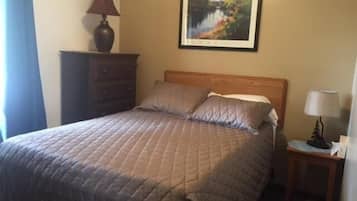 Una cama bien tendida con una colcha acolchada, un cabecero de madera y un cuadro enmarcado en la pared de arriba.