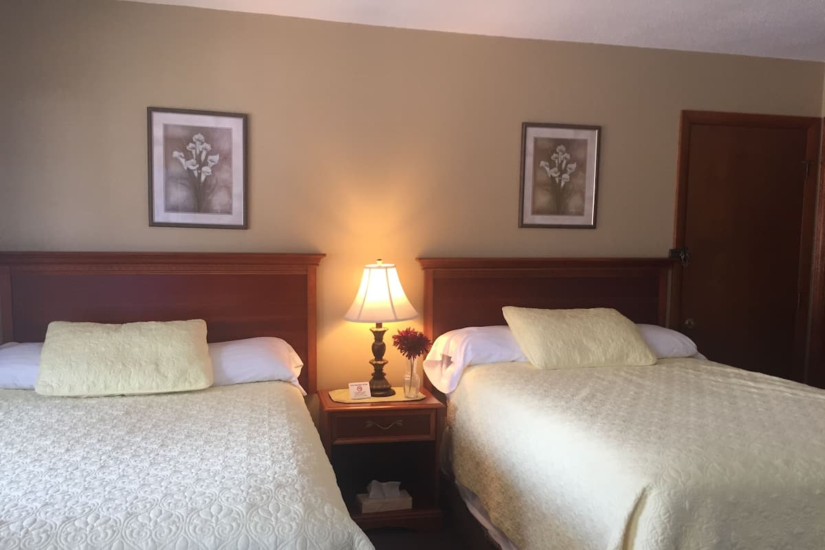 Ein Hotelzimmer mit zwei Betten, einem Nachttisch mit Lampe sowie zwei gerahmten Blumenbildern an der Wand.