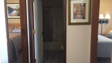 Ein Hotelzimmer mit Bett, einem Badezimmer mit Dusche und einem Flur, der zu einem weiteren Zimmer führt.