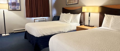 A hotel room with two beds, a nightstand, a lamp, and a wall-mounted air conditioning unit.