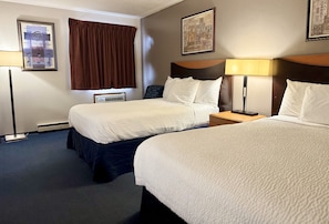 A hotel room with two beds, a nightstand, a lamp, and a wall-mounted air conditioning unit. - Travel Inn (Watertown)