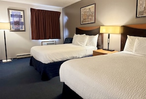 Habitación de hotel con dos camas, una mesita de noche, una lámpara y un aire acondicionado instalado en la pared.