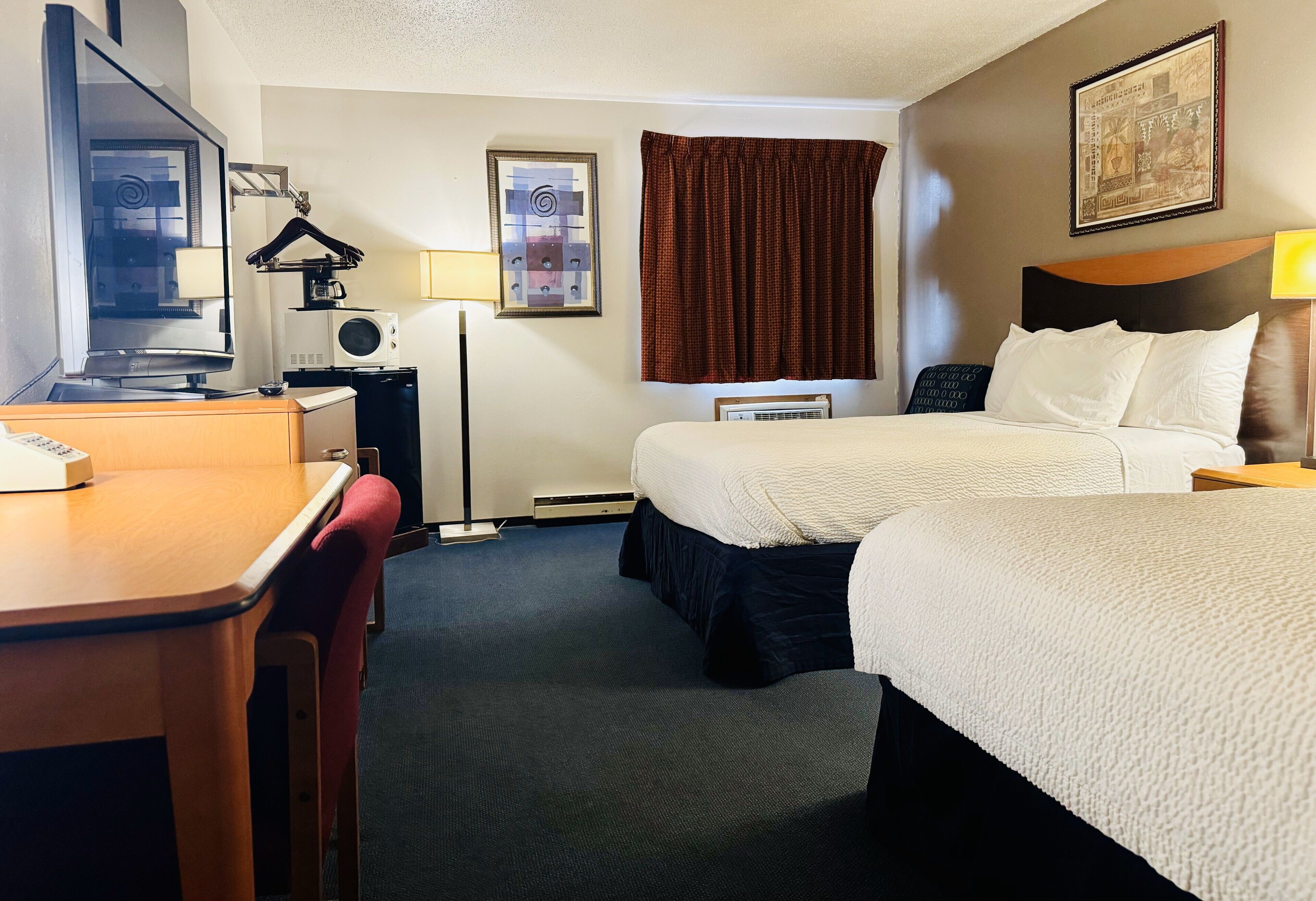 A hotel room with a desk, two beds, a television, a microwave, and a framed picture on the wall.