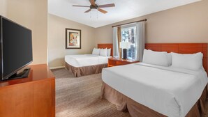 Ein Hotelzimmer mit zwei Betten, einem Fernseher, einem Deckenventilator und einem Fenster mit Vorhängen.