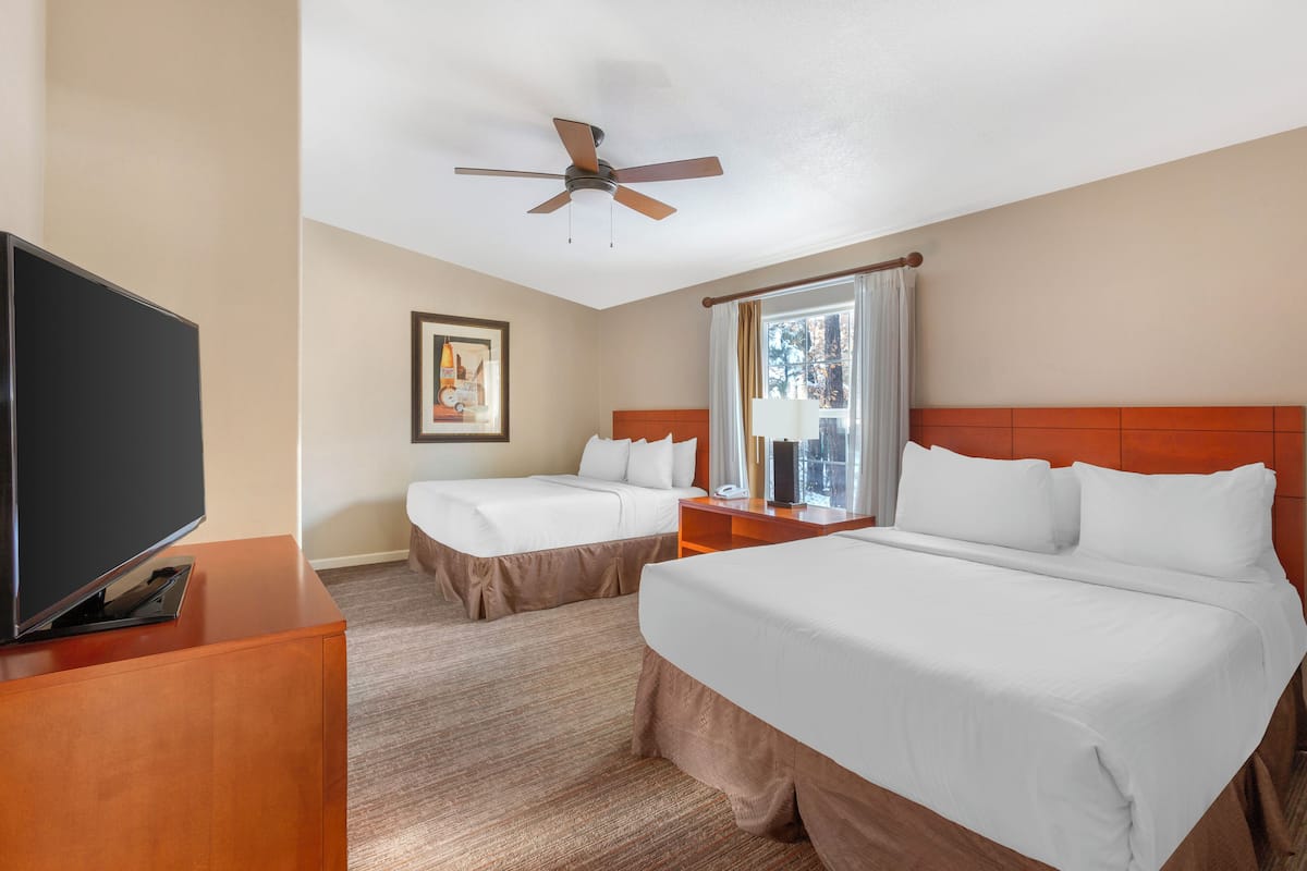 A hotel room with two beds, a TV, a ceiling fan, and a window with curtains.