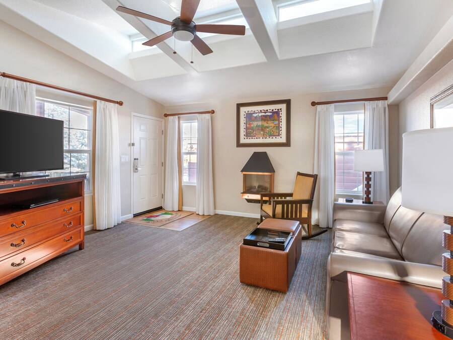 A spacious living room with a flat-screen TV, a ceiling fan, a sofa, a coffee table, and a lamp.