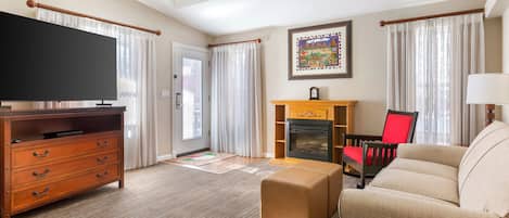 A living room with a flat-screen TV, wooden furniture, a fireplace, and a ceiling fan.