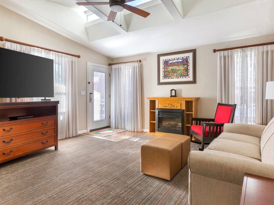 A living room with a flat-screen TV, wooden furniture, a fireplace, and a ceiling fan.