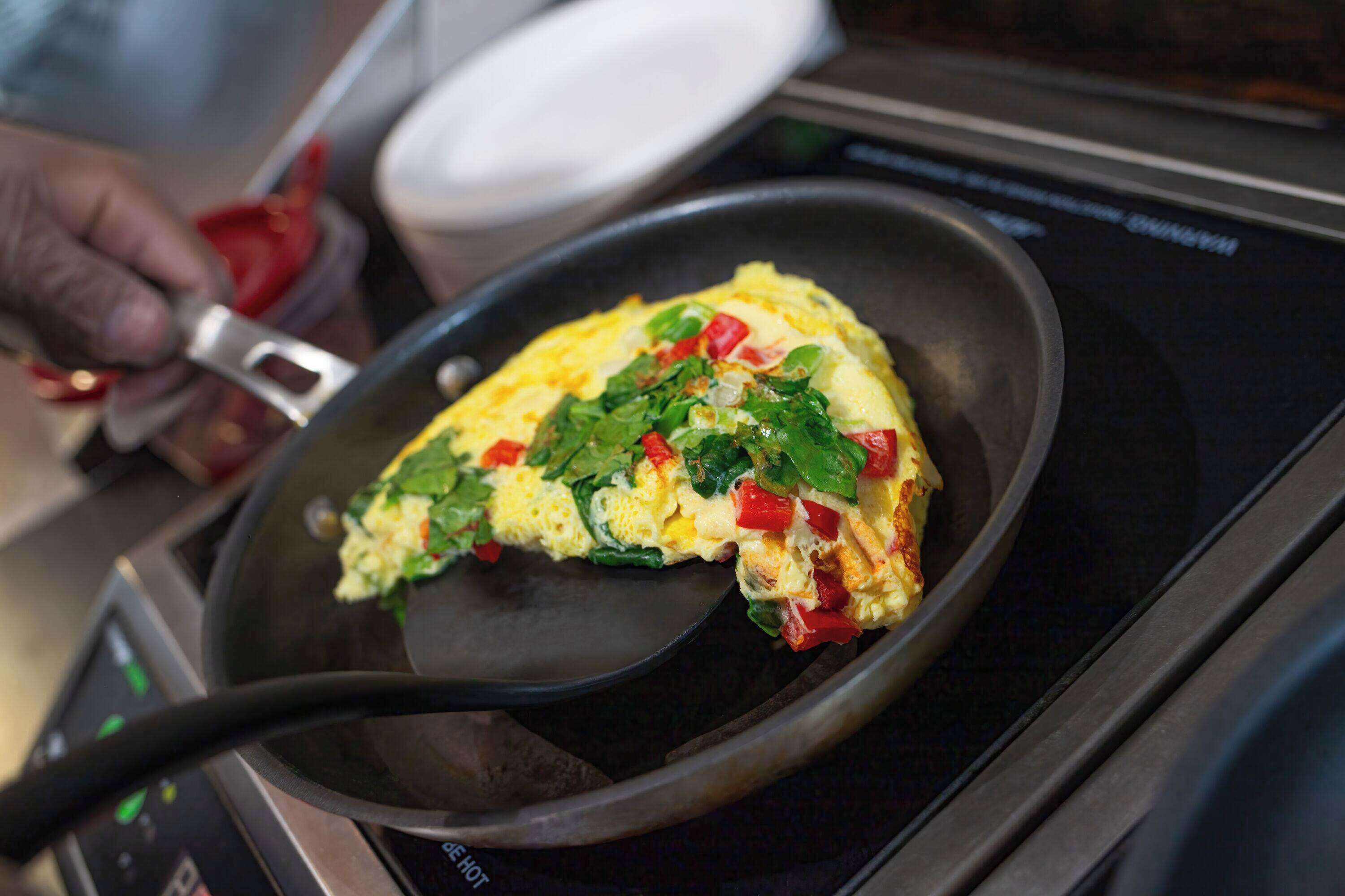 A person cooking an omelette in a non-stick pan on an induction cooktop.