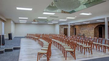 Un salón de conferencias con filas de sillas de madera, suelo alfombrado y una pared de ladrillo con un arco.