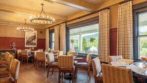 A dining area with wooden tables and chairs, large windows with curtains, and hanging light fixtures. - Eagle Mountain House & Golf Club (Jackson)